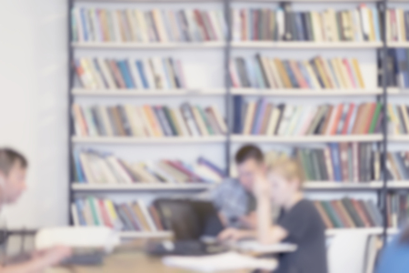 Abstract unrecognizable studenten in public library, in reading room. Blurred bookshelves of bookcase with books, studing, education. Light filter effect, soft focusの写真素材