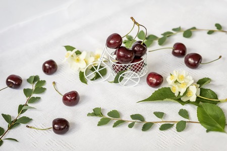 Miniature toy shopping cart, trolley with ripe cherry, jasmine flowers, green foliage on light background. Concept of healthy food, detox, vitamins, dietingの写真素材