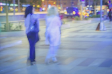 Abstract defocused motion blurred young girls , blurred background, unidentified people, city street in evening. Vivid illumination. Concept of seasons, weather, modern cityの写真素材