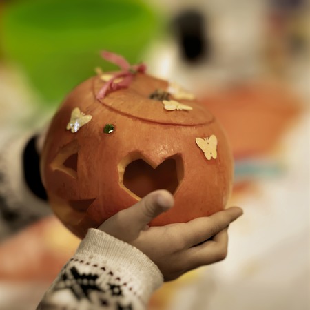 Childrens hands with decorative carved and decorated pumpkin. Traditional symbol for harvest holidays, Thanksgiving Day, Halloween. Decoration of home family holidaysの写真素材