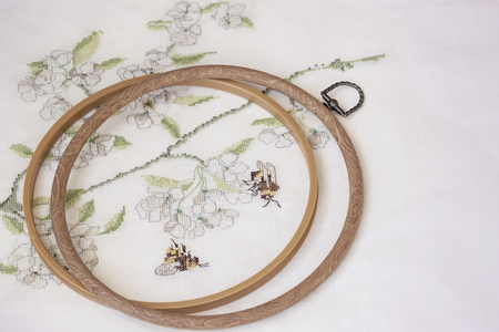 Wooden embroidery hoop with fragment of a colorful cross-stitch embroidery on fabric close-up, summer ornamentの写真素材