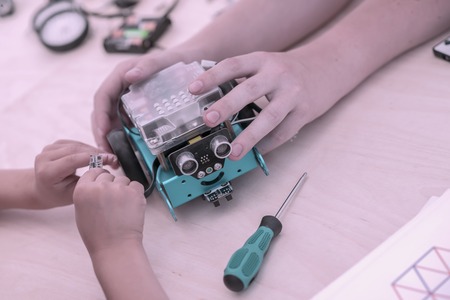 Hands of children gathering a model of controlled all-terrain vehicle, home-made robotic toy. Concept of childrens hobby, learning, technology, learning, engineeringの写真素材