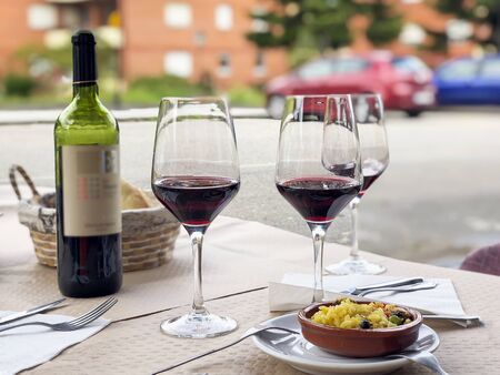Three glasses of red wine, bottle of wine and chefs compliment, small plate of paella served on...