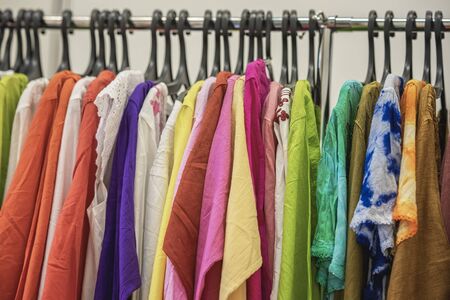 Colorful clothes on hangers for sale in shop. Summer season, assortment in a clothing store. Choice of cotton clothes of different colors on hangersの写真素材