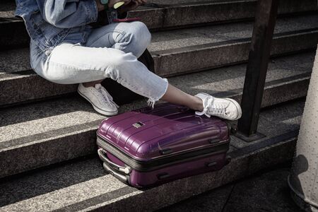 Unrecognizable young girl student sitting resting on the steps with a suitcase, youth travel and...
