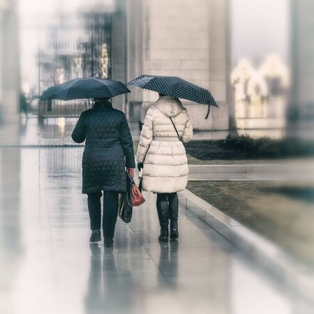Two elderly women under umbrellas backs to us, lifestyle in the cityの写真素材