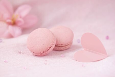 Pair of pink macaroons closeup, heart and flowers, romantic delicate pastel background. Concept of...
