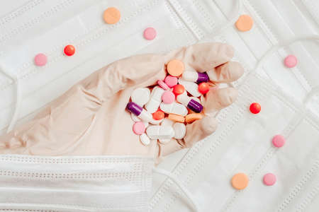 Hand in protective glove with pills of different colors and sizes on background of disposable protective medical masks, hygiene and health protect ill, flat lay, top view. Concept of health, pharmaceutical industry, medicine, treatmentの写真素材