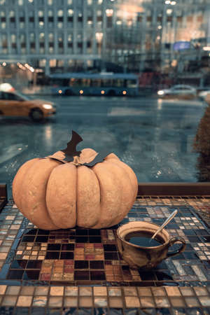Holiday symbol, decor, halloween natural pumpkin with carved paper black bats and cup of coffee, twilight, street window viewの写真素材