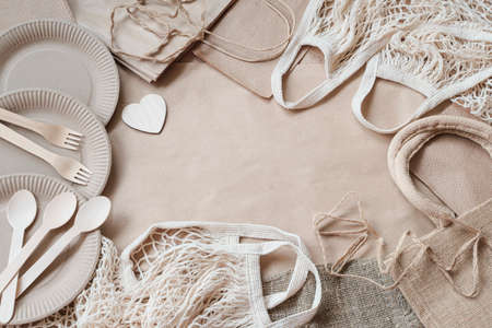 Zero waste. Set of eco produce, plastic-free, neutral color, ecology concept. Paper disposable tableware, wooden cutlery and heart, reusable cotton mesh bag, top view, flat layの写真素材