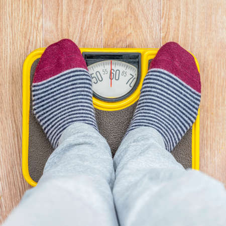Close-up of legs in socks stepping on floor scales. Weight measure, food control, healthy care conceptの写真素材