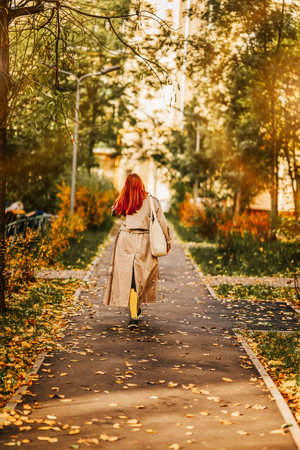 Autumn day, walk in city among the fallen leaves. Unrecognizable red-haired, bright girl, rear viewの写真素材