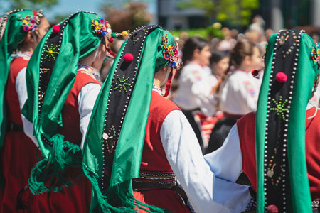 Rear view on Bulgarian dancers in traditional national costumes dancing outdoors, selective focus