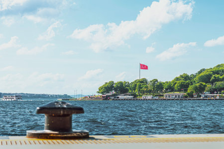 Red Turkish flag waves proudly atop a tall pole in the Bosphorus Strait on a Sunny Day