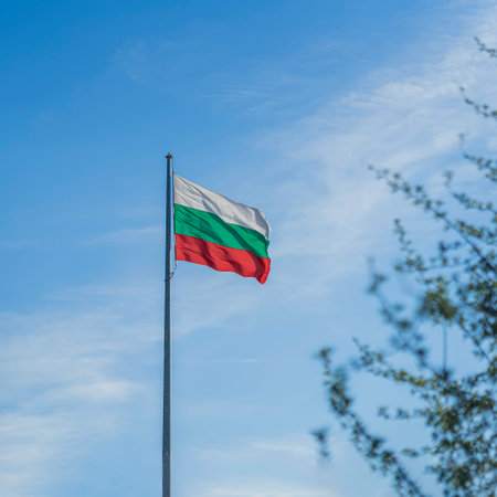 National flag of Bulgaria on a flagpole in front of blue sky with clouds