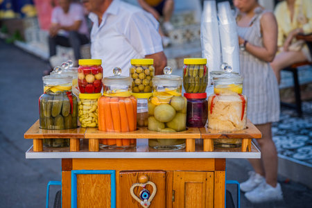 Colorful jars of pickled vegetables displayed on a wooden cart at a bustling marketの写真素材