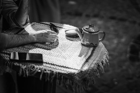 Tranquil afternoon tea gathering featuring a hand over a table with kettle and cup in a sunlit outdoor settingの写真素材