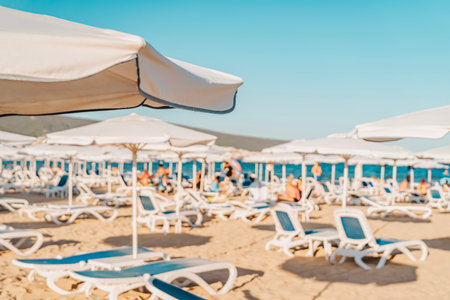 Sunny beach day with lounge chairs and umbrellas, relaxation, summer shoreline. Abstract blurred backgroundの写真素材