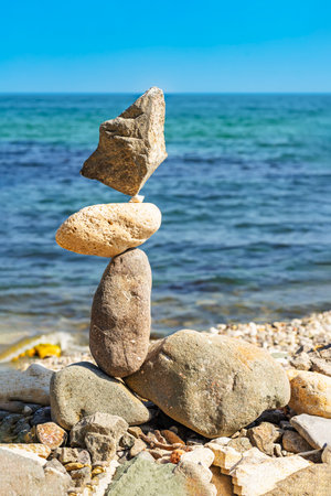 Balanced stone sculpture, rocky shore, tranquil sea in sunny dayの写真素材