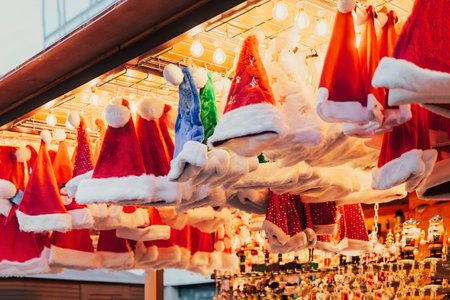 Bright display of red and white Santa hats with festive lighting at Christmas market stallの写真素材