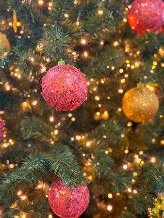 Shiny pink Christmas ball with sequin texture hanging on decorated tree. Elegant holiday decor