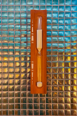 Wooden sand timer for sauna mounted on a glass mosaic wall. Traditional timekeeping device for steam...