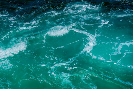 Top view of turquoise ocean waves crashing with white foam in sunlight. Ocean water symbolizes nature, motion, freedomの写真素材