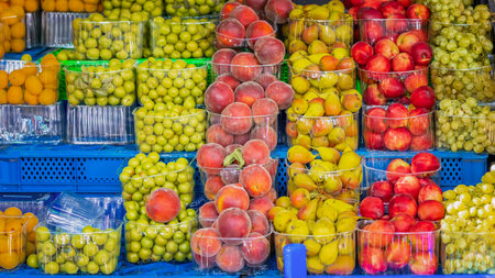 Colorful fresh fruit display at local market, peaches, plums, apples, and grapes in clear containers. Fruits in plastic trays highlight local produce diversityの写真素材