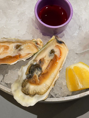 Fresh oysters served on crushed ice with red sauce and lemon slice in modern seafood restaurant...