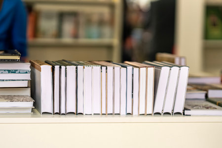 Stack of hardcover books lined up on white shelf in bookstore environment. Concept of books, reading...