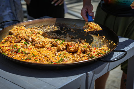 Traditional chicken paella in large skillet served fresh outdoors with vibrant ingredients and golden rice. Concept of paella, Spanish cuisine, authentic street food experienceの写真素材