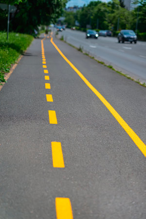 Bicycle lane marked with yellow line runs along city sidewalk. Urban bike path marked with yellow dashed and solid lines along gray asphalt surface. Concept of transportation, safety, active mobilityの写真素材