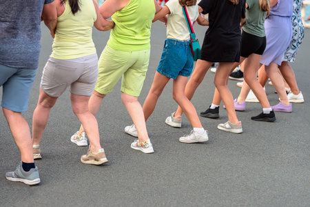 Mixed group of people dancing horo in line outdoors, linked by arms outdoor. Concept of dancing,...