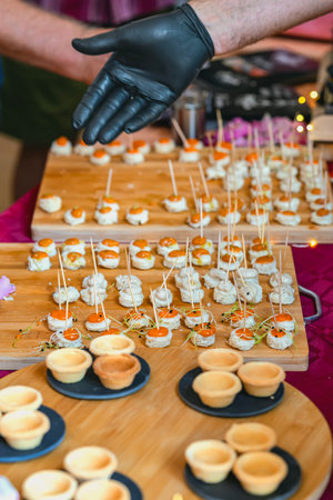 Mini canapes on wooden boards with toothpicks and chefs gloved hand presenting appetizers at food...
