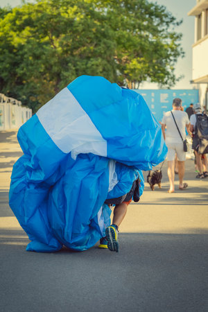 Man carrying parachute after flight. Paraglider carries large folded parachute on street after...