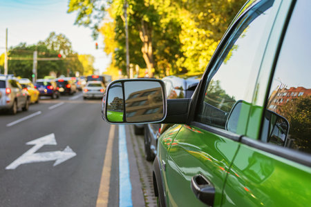 Green car parked by urban street with heavy city traffic and sunlight reflections. Concept of traffic, driving and car transportationの写真素材