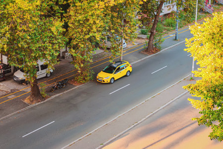 Yellow car parked alone on urban street under trees during sunny autumn afternoon. Concept of urban solitude, mobility and seasonal cityscapeの写真素材