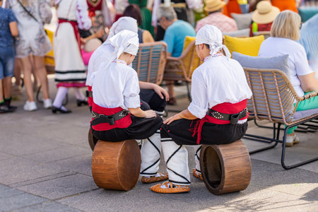 Folk Bulgarian musicians, dancers performing with authentic drums. Three person in traditional folk costumes sitting on wooden drums at cultural fest. Concept of folklore, tradition, art performanceの写真素材