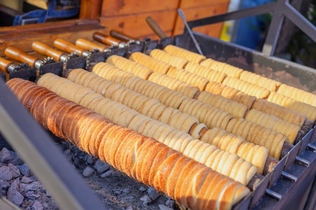 Traditional trdelnik pastries are roasting on rotating wooden spits over hot coals. Concept of trdelnik as a sweet street food, concept of trdelnik as cultural dessertの写真素材