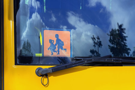 Orange school bus with of School Going Children sign visible through windshield with blue sky reflection. Concept of road safety, school transport, child protectionの写真素材
