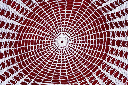 White crochet doily in circular geometric pattern placed on red background. Concept of handmade art,...