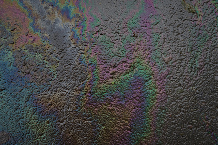 Oil slick with dark rainbow colors on wet asphalt symbolizing urban pollution, environmental...