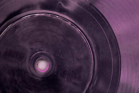 Close-up of old vinyl record or plastic disc with scratches, spots and cracks, in purple hue. Concept of retro music, abstract vintage sound background or grainy analog textureの写真素材