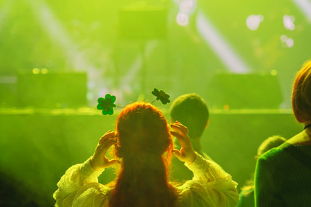 Woman wearing shamrock headband dancing at club party with green lights and Irish vibes. Concept of St. Patrick Day celebration, fun, cultural spiritの写真素材