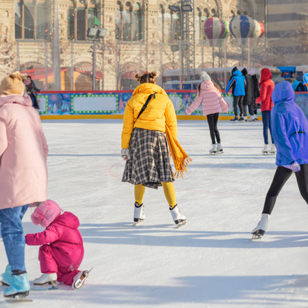 City skating rink. Crowd of people skating on festive outdoor ice rink during winter holiday in city center. Concept of seasonal celebration, urban joy, family funの写真素材