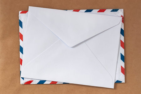 White envelope placed on airmail envelope isolated on paper background, copy space. Postal communication concept. Envelope messaging, mail delivery, business correspondence, minimal mockup background