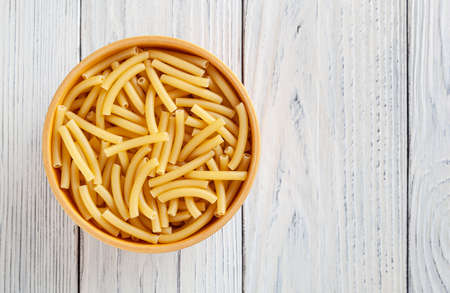 Uncooked maccheroni pasta in wooden bowl on white wooden backgroundの写真素材
