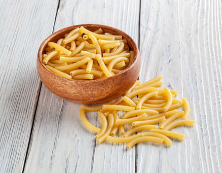 Uncooked maccheroni pasta in wooden bowl on white wooden backgroundの写真素材