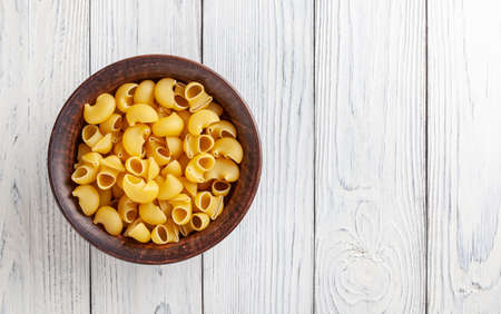 Uncooked pipe rigate pasta in ceramic bowl on white wooden background