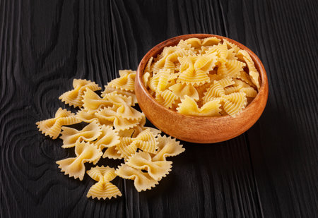 Uncooked farfalle rigate pasta in wooden bowl on black wooden backgroundの写真素材